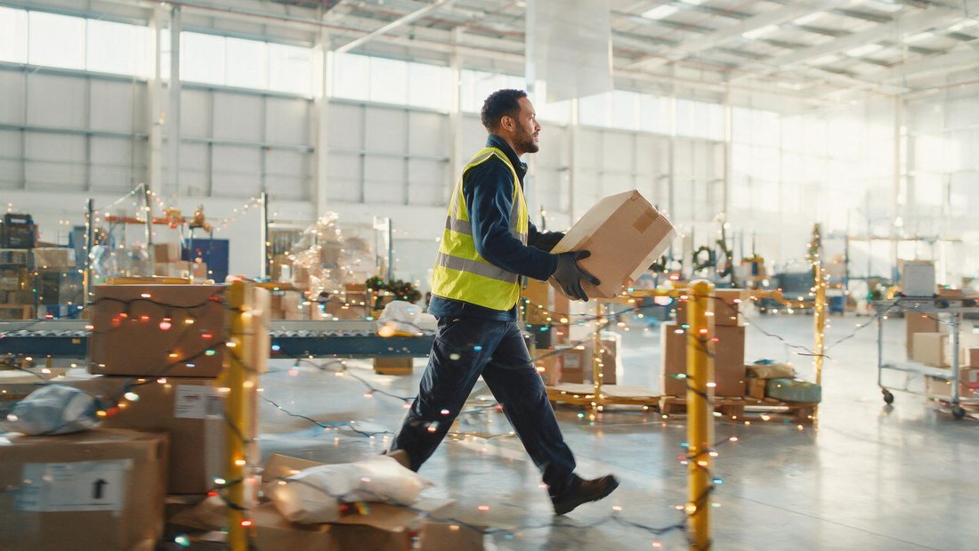 Warehouse worker moving parcels past festive lights in a bright modern depot