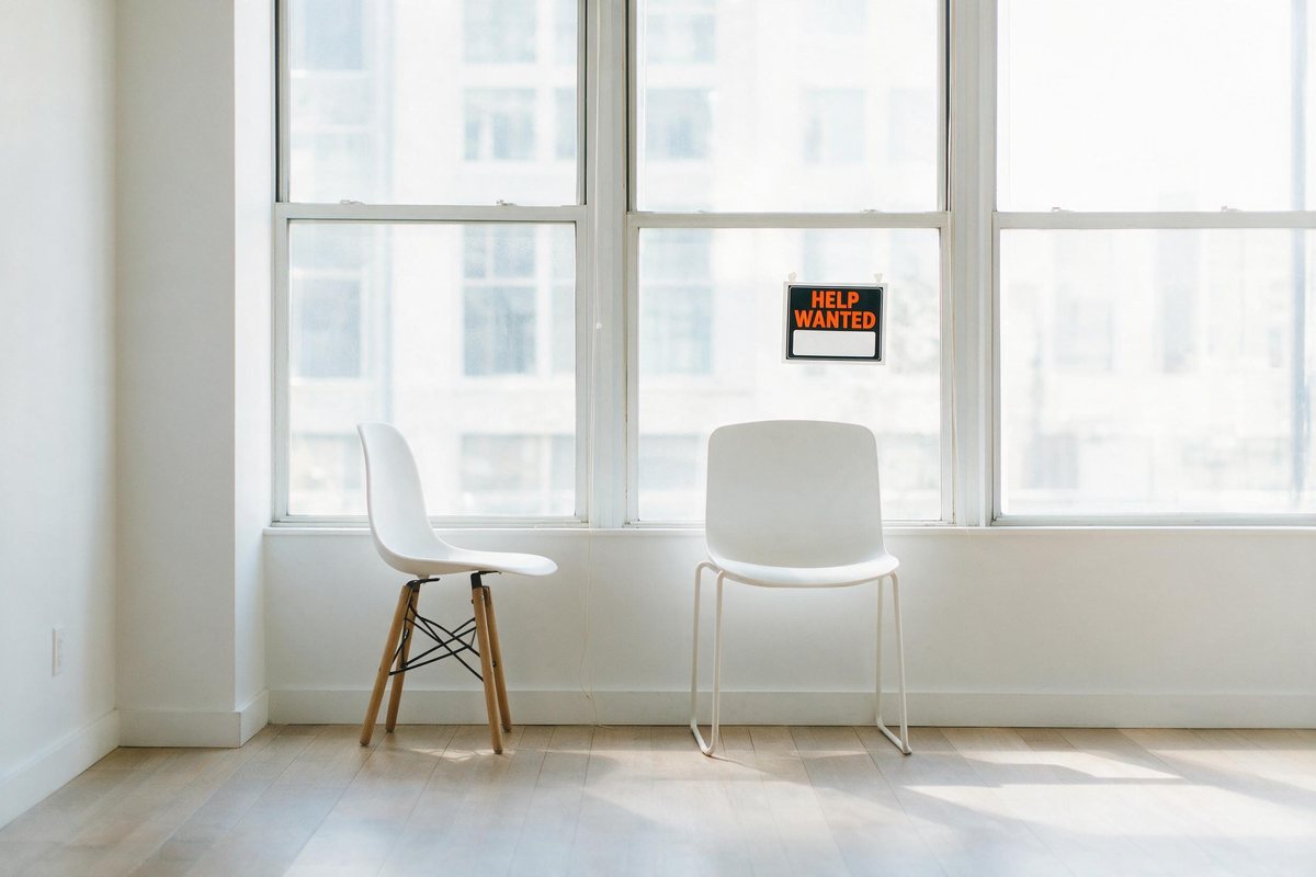 Empty bright office chairs beside a window with a help wanted sign on the glass